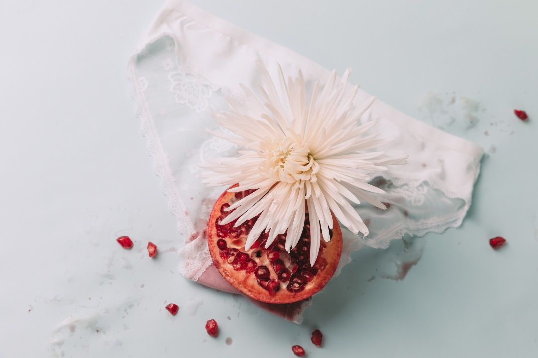 Granada y flor sobre ropa interior femenina como metáfora visual del ciclo menstrual y la energía femenina en la escalada