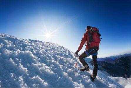 Montañero caminando sobre nieve con piolet en alta montaña, representando el impacto del clima frío en el rendimiento y la nutrición deportiva