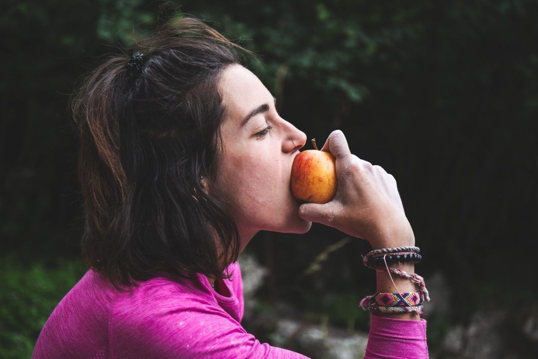 Mujer comiendo una manzana, representando la importancia de comer algo durante una jornada de escalada.