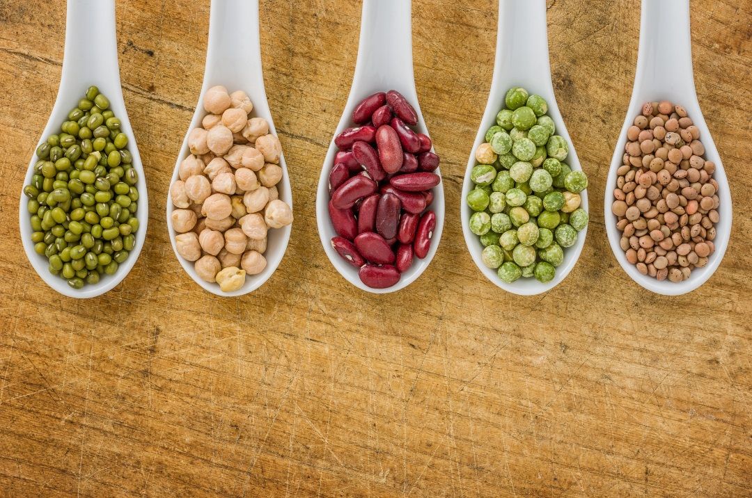 Variedad de alimentos vegetales sobre una mesa: legumbres, verduras, tofu, frutas y semillas, representando una dieta vegana equilibrada.