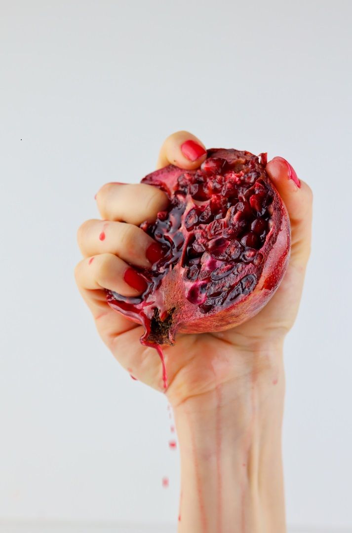 Mano exprimiendo una granada roja, alimento rico en antioxidantes útil durante el ciclo menstrual