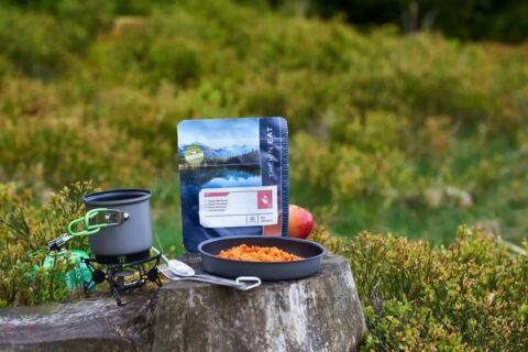 Plato con comida preparada junto a un hornillo de camping y una bolsa de comida deshidratada, ejemplo de alimentación práctica para expediciones en montaña